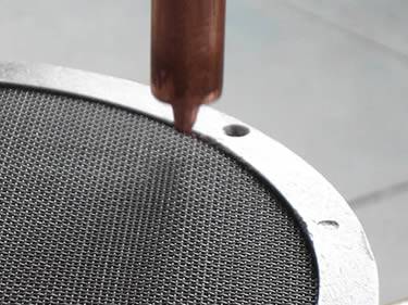 A filter disc is under a spot welding tool.
