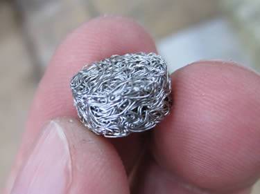 A mini round compressed knitted mesh filter made by stainless steel wire on a man fingers.