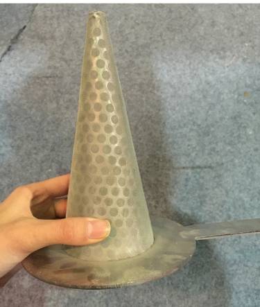 A worker is holding a perforated conical strainer with sharp bottom.